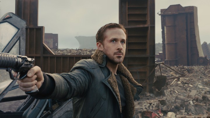 K apontando uma arma para a direita, mas olhando para a frente em um terreno baldio em Blade Runner 2049.