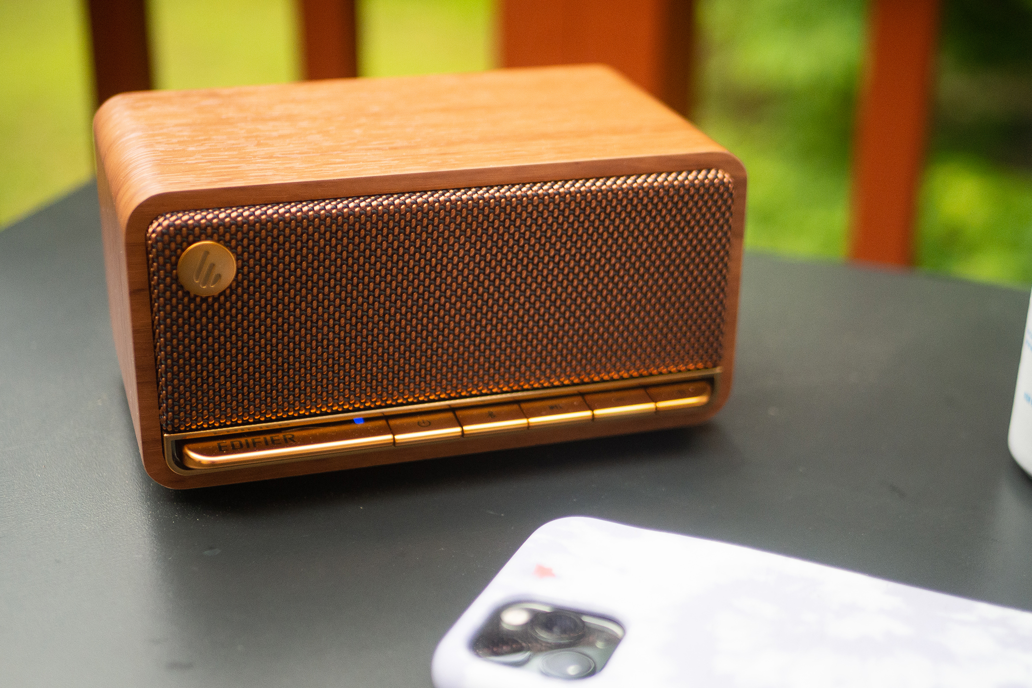 The Edifier MP230 speaker is sitting on a table on a porch next to an iPhone 11 Pro