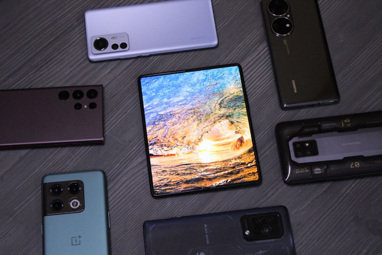 จอแสดงผลด้านในของ Galaxy Z Fold 3 ที่วางคู่กับโทรศัพท์รุ่นเรือธงอื่นๆ บนโต๊ะ