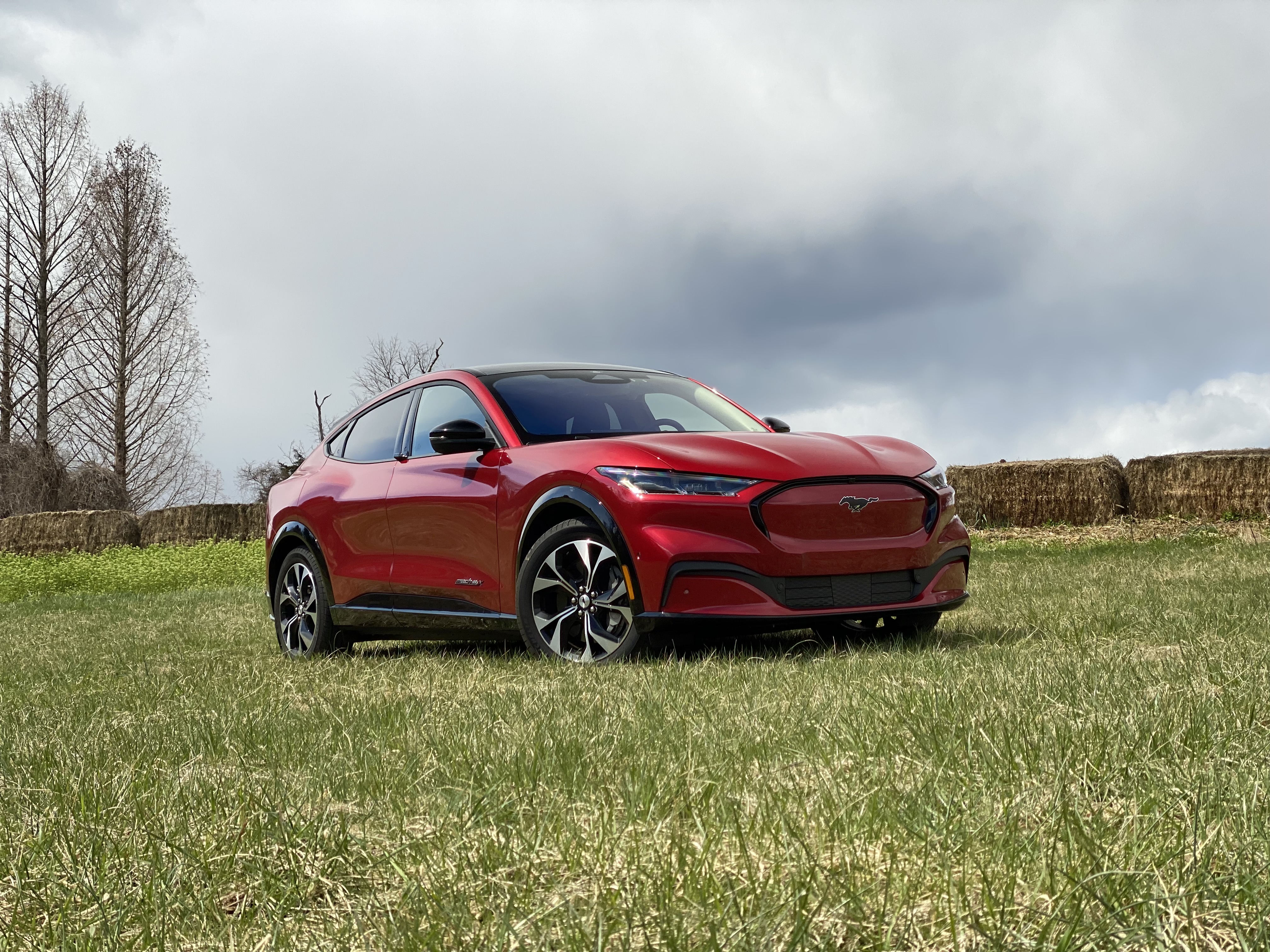 2021 Ford Mustang Mach-E from the front passenger side in a grassy field with dark clouds in the back.