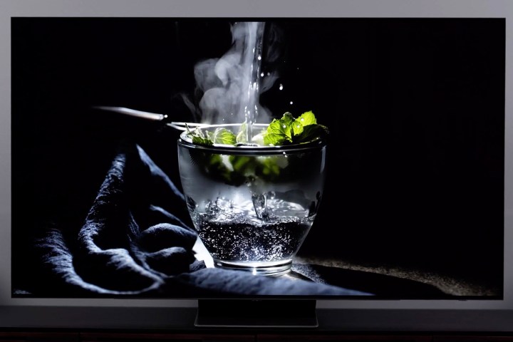 The Samsung S95B OLED displays a picture hot water being poured into a glass against a dark background.