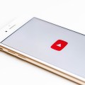 Красно-белый логотип YouTube на экране телефона. Телефон на белом фоне.