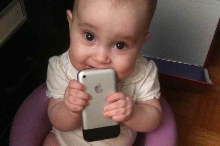 Baby girl holding 2007 iPhone to her mouth.
