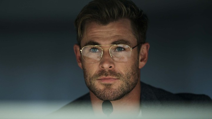 Chris Hemsworth smirks in front of a mi crophone in a scene from Spiderhead.