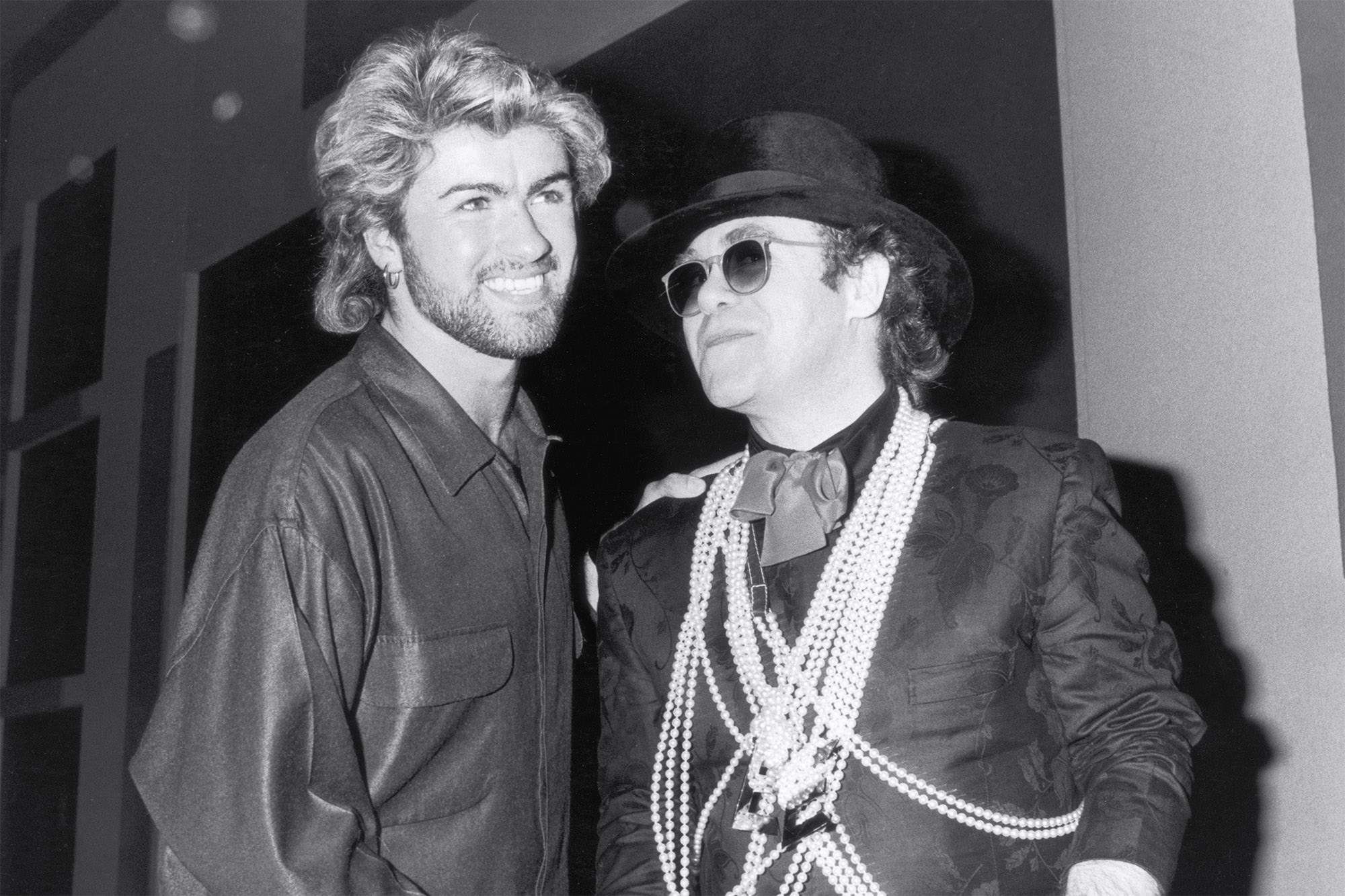 A estrela pop Elton John (à direita) parabeniza George Michael por ganhar o prêmio Ivor Novello Songwriter of the Year no Grosvenor House Hotel, em Londres, em 13 de março de 1985.