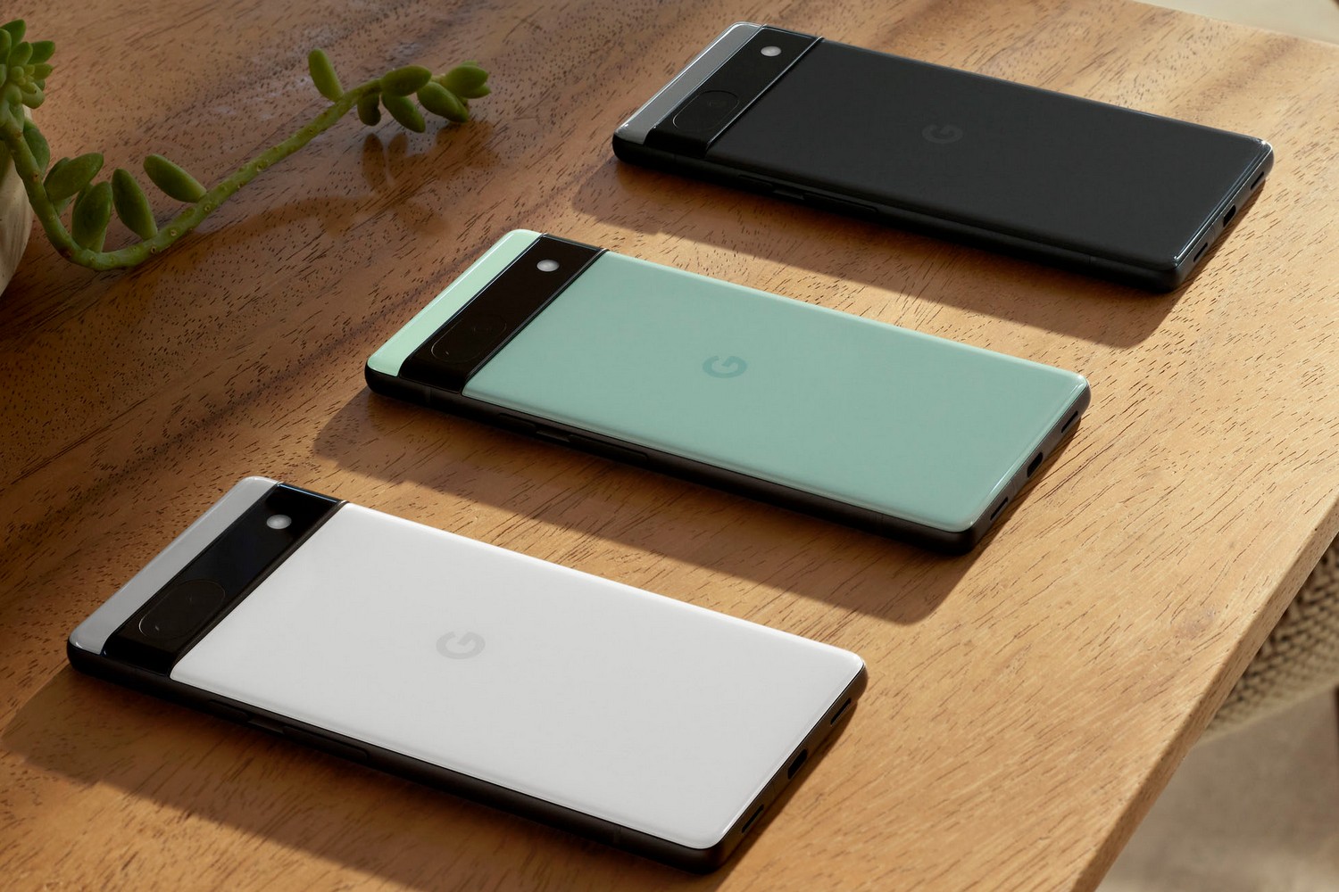Três smartphones Google Pixel 6a em três cores estão virados para baixo sobre uma mesa.