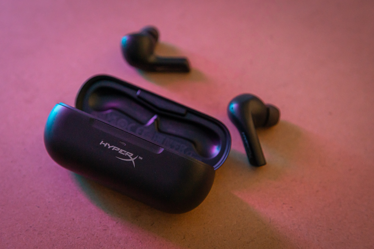 HyperX Cloud Alpha earbuds sitting outside their case on a table.