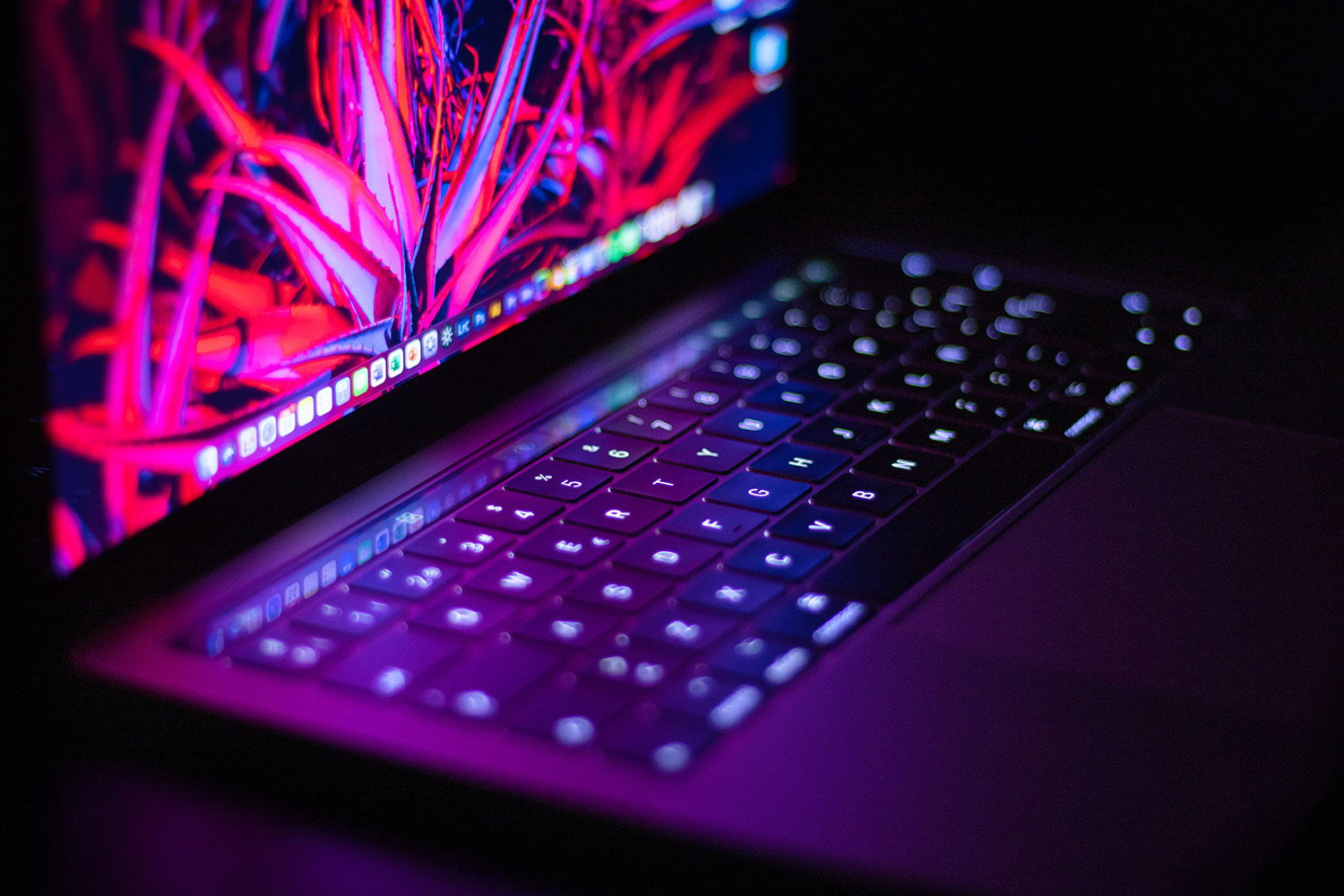 A close-up of a MacBook illuminated under neon lights.