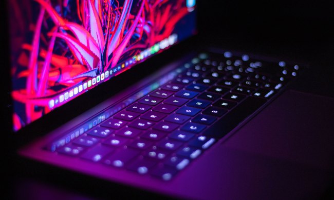 A close-up of a MacBook illuminated under neon lights.