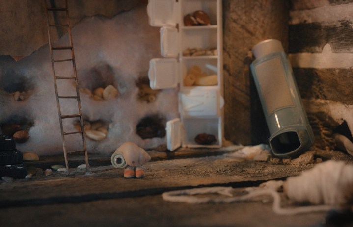 Marcel the Shell se tient dans une petite pièce remplie de petits articles ménagers qu'il a récupérés, dont un inhalateur.