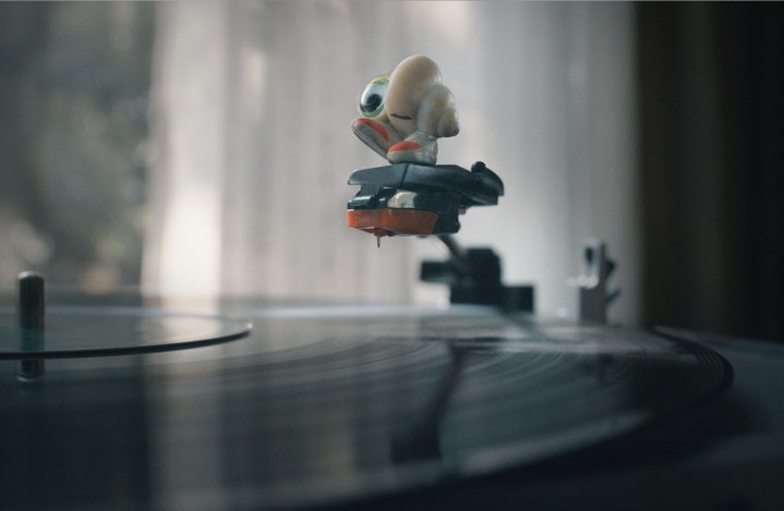 Marcel the Shell stands on the record player's needle, smiling.