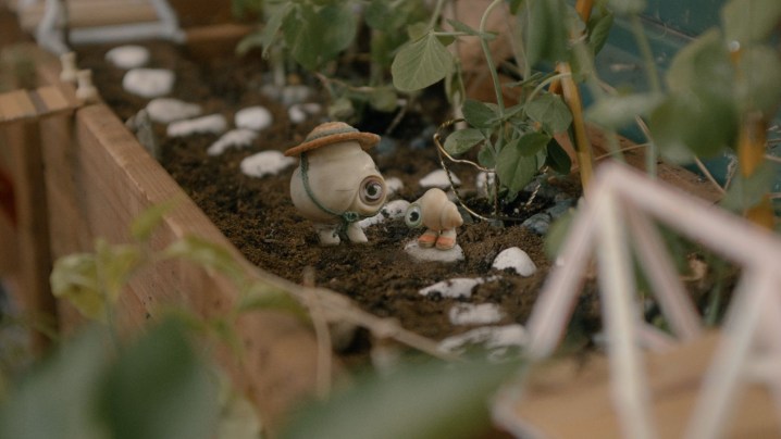 Marcel the Shell and his grandmother, Connie, stand in a tiny garden bed lined with stones.