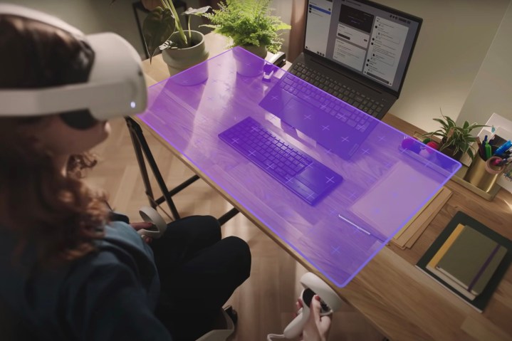 A woman sits at her desk with a VR headset on, working in the Metaverse.
