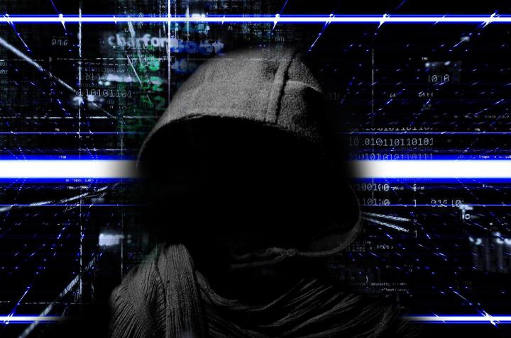 a faceless hacker in a black hoodie in front of a computer screen with lines of code on it