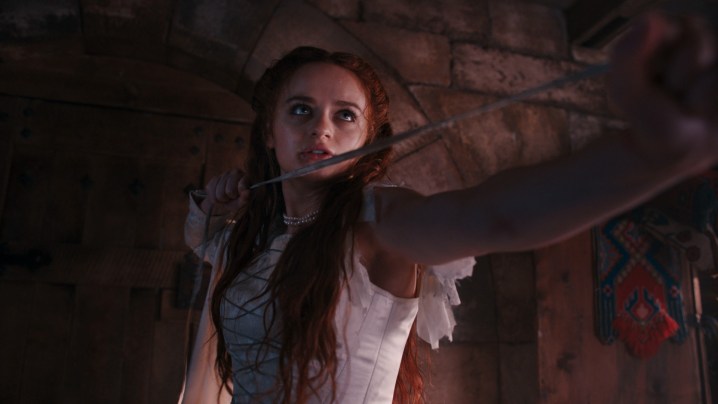 Joey King stands in the shadows, holding a sword, in a scene from The Princess.
