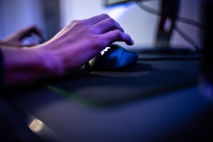 Mão em um mouse de computador, iluminação roxa.