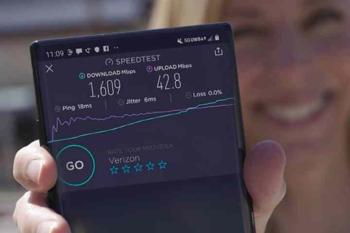 Женщина держит смартфон с результатами теста скорости в сверхширокополосной сети Verizon 5G.