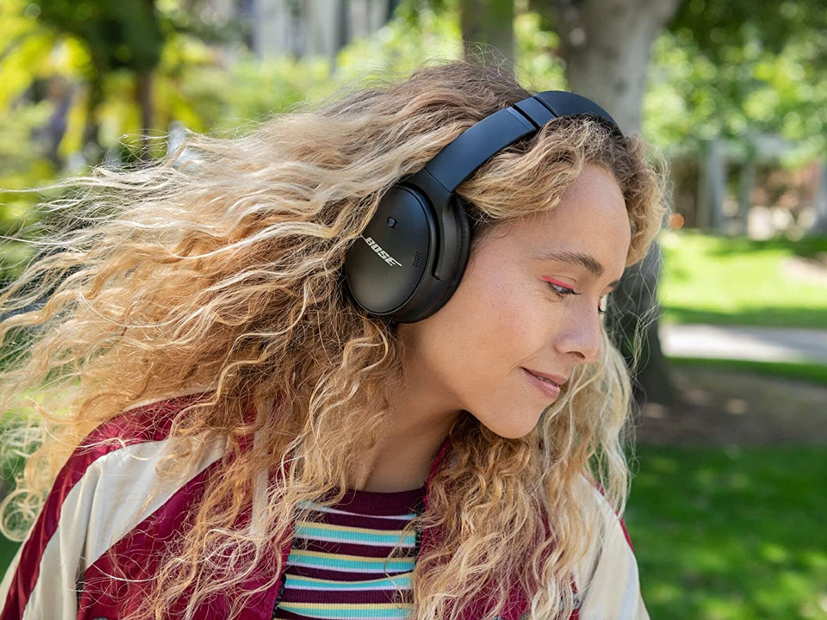 Uma mulher em um parque usando fones de ouvido com cancelamento de ruído sem fio Bose QuietComfort 45 Bluetooth.