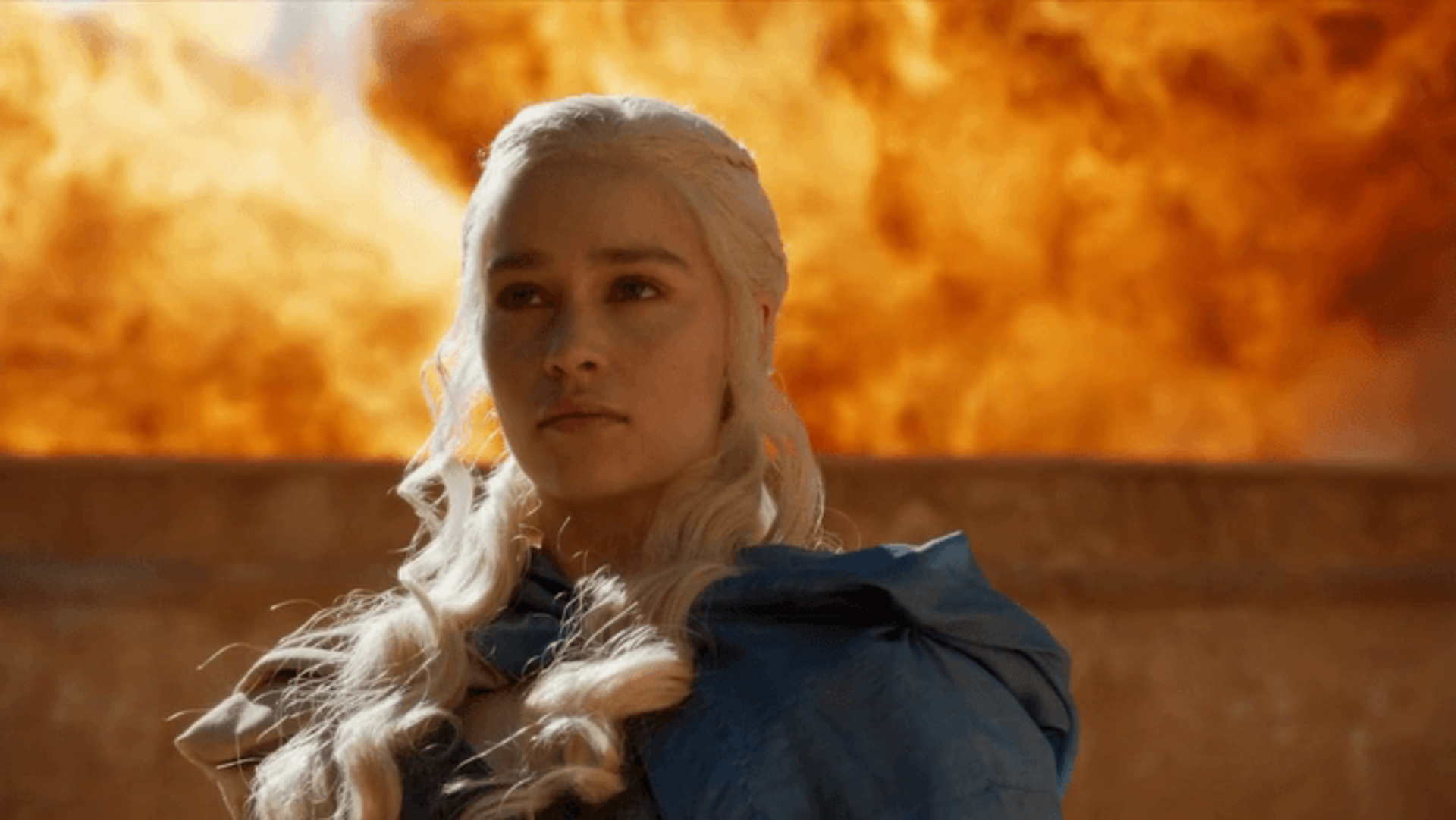 Uma Daenerys severa com uma explosão do fogo de Drogon ao fundo.