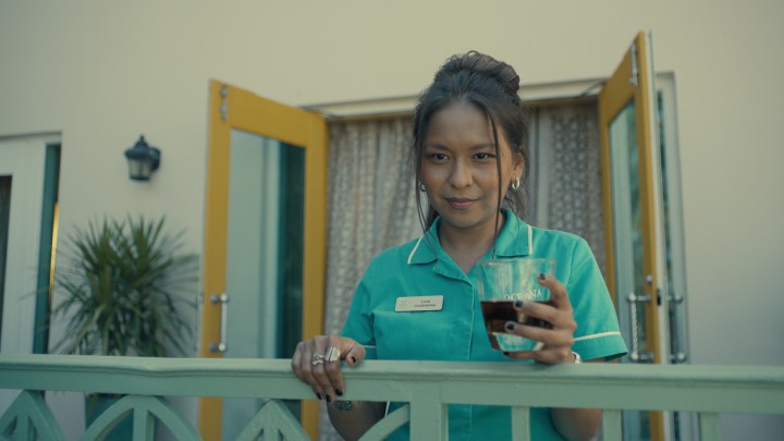 Gabriela Cartol segurando uma bebida na varanda de um hotel em cena de The Resort.