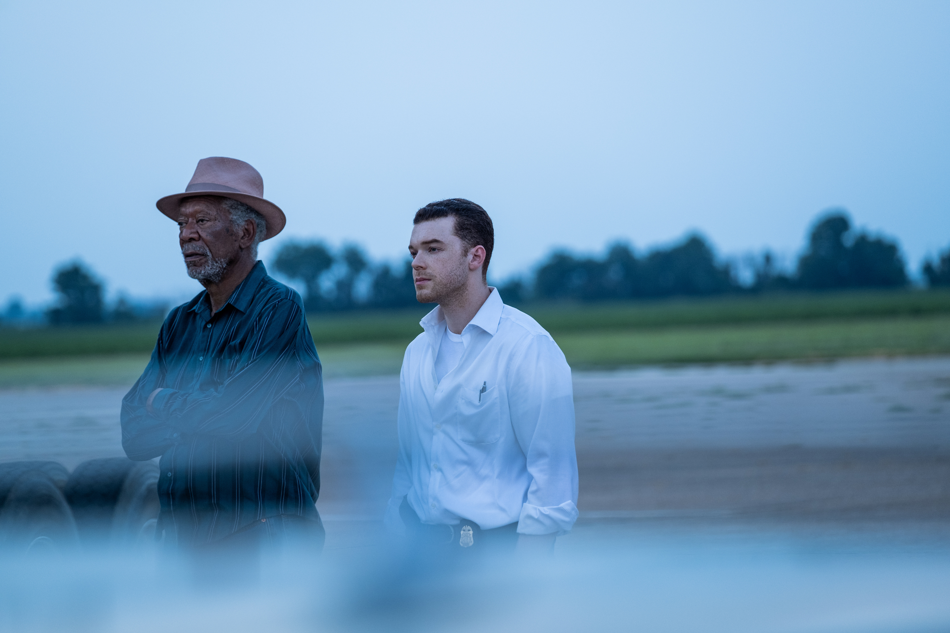 Morgan Freeman y Cameron Monaghan se paran uno al lado del otro y miran a lo lejos en una escena de Paradise Highway.