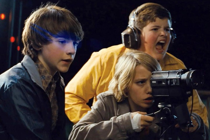 The main characters from Super 8 are filming something with a camera and screaming excitedly.