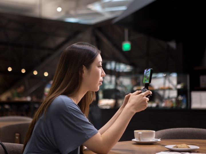 Woman playing games on a smartphone with GeForce Now in coffee shop.