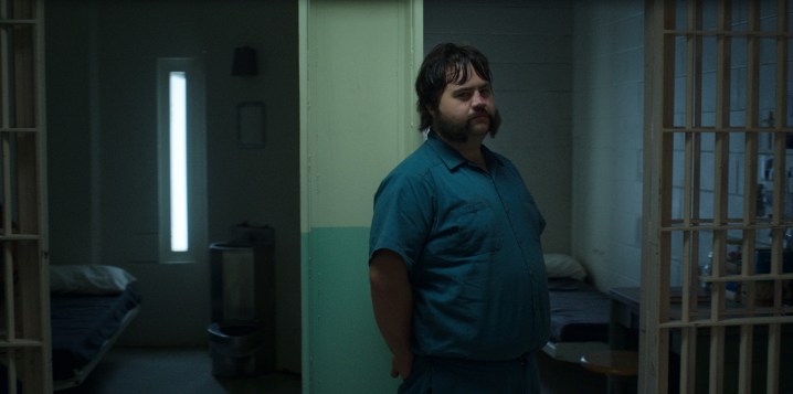 Paul Walter Hauser leans against the door of his character's prison cell in a scene from Black Bird.