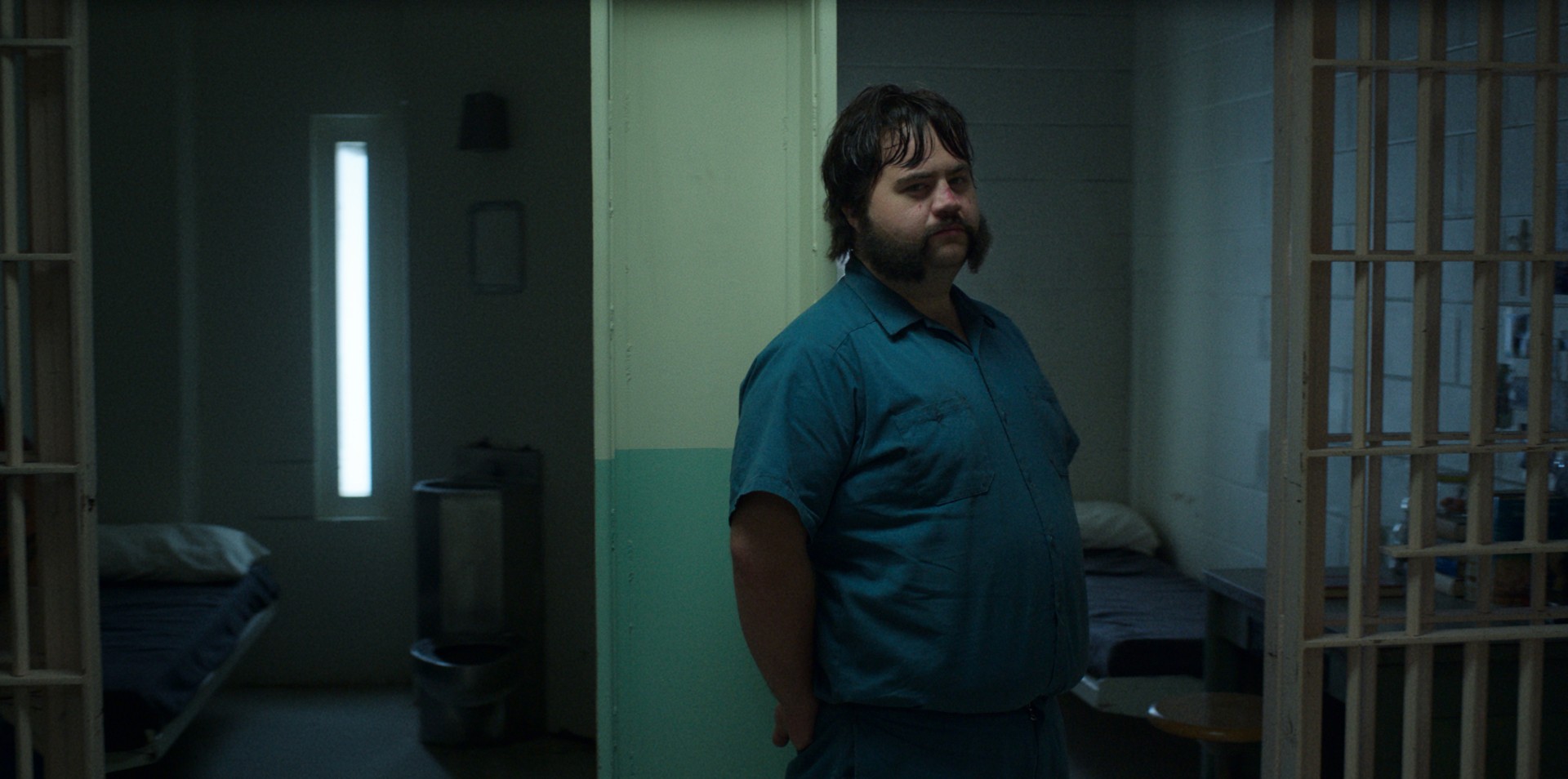 Paul Walter Hauser se encosta na porta da cela de seu personagem em uma cena de Black Bird.