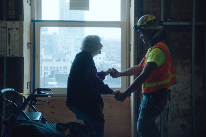 Seorang wanita tua menari dengan seorang pekerja konstruksi di Dreaming Walls.