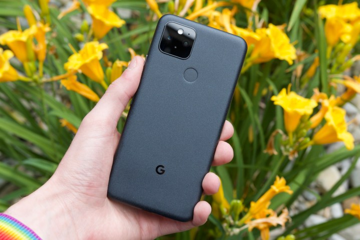 Someone holding the Google Pixel 5.  In the background are yellow flowers, slightly out of focus.