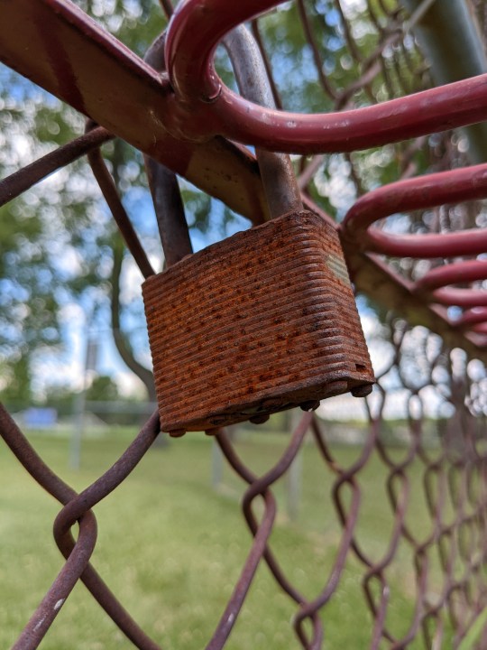 Un vecchio lucchetto arrugginito attaccato a una recinzione a maglie di catena.