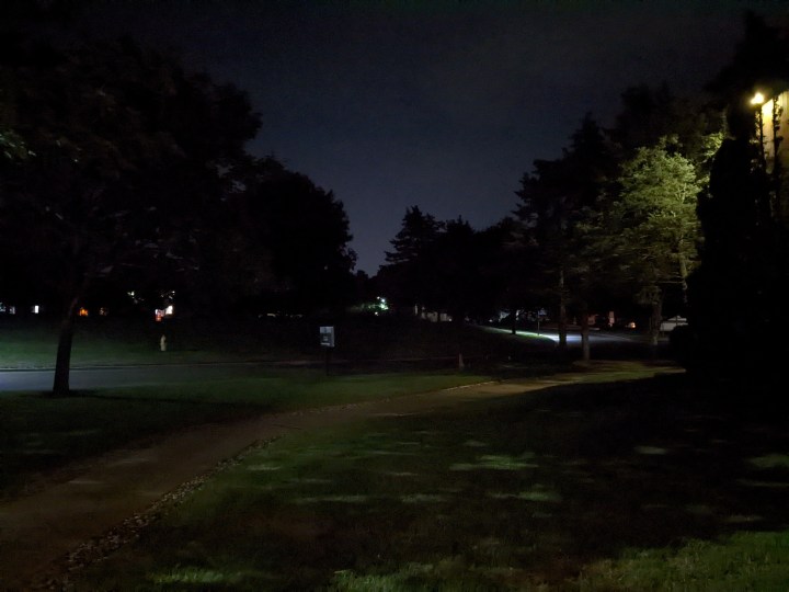 Una foto molto scura di notte. Riesci a malapena a distinguere un marciapiede e alcuni alberi.