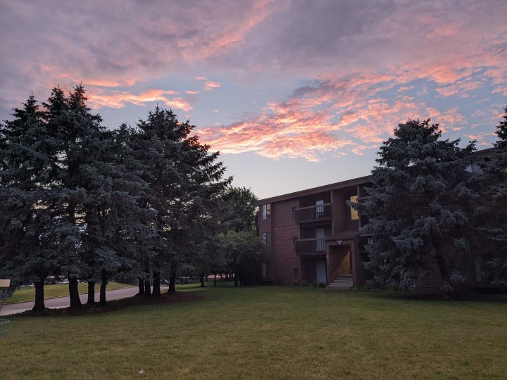 Un condominio circondato da alberi. Sopra c'è un cielo azzurro e rosa al tramonto.