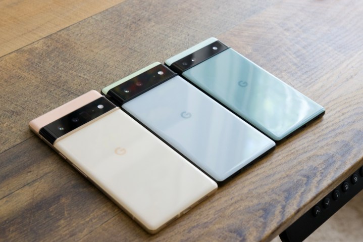 The Google Pixel 6 Pro, Pixel 6, and Pixel 6a all lined up on a wooden desk.