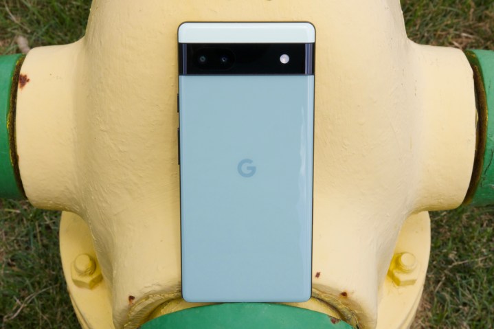 Google Pixel 6a resting against a yellow fire hydrant.