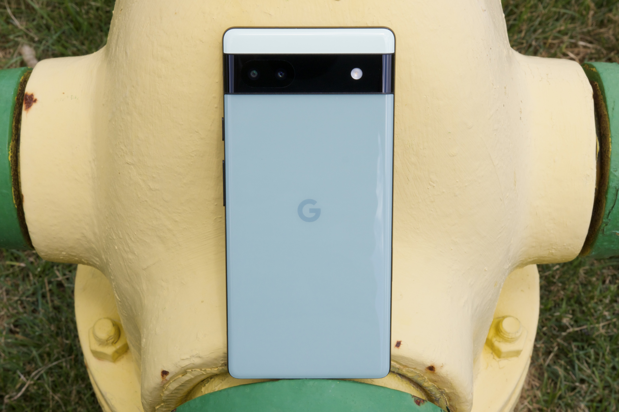 Google Pixel 6a resting against a yellow fire hydrant.