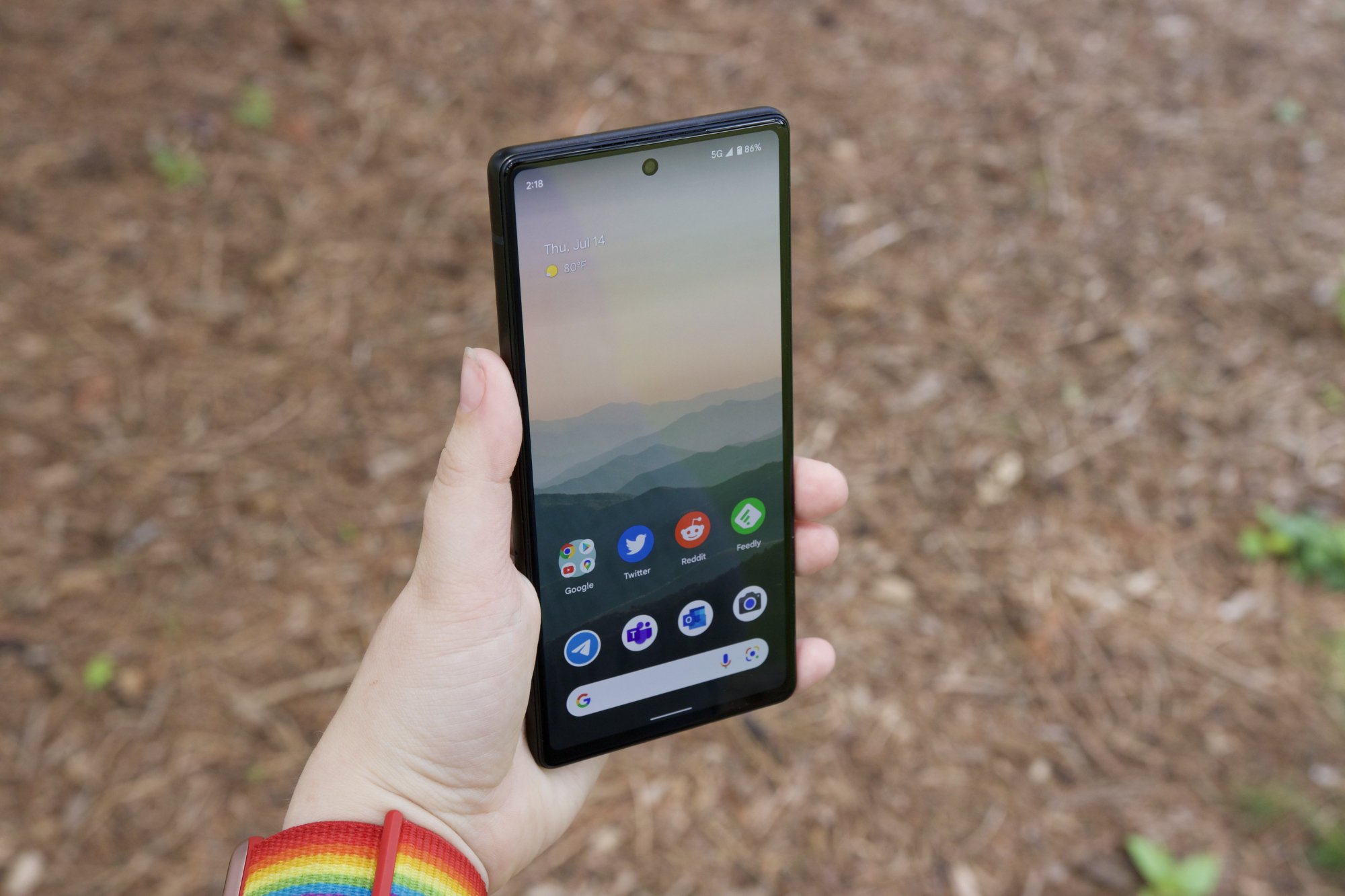 شخصی یک Google Pixel 6a در دست دارد.  صفحه نمایش روشن است و صفحه اصلی گوشی را نشان می دهد.