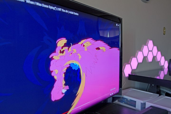 Lampade da parete Govee Glide Hexa che rispecchiano i colori di un'immagine su un televisore vicino.