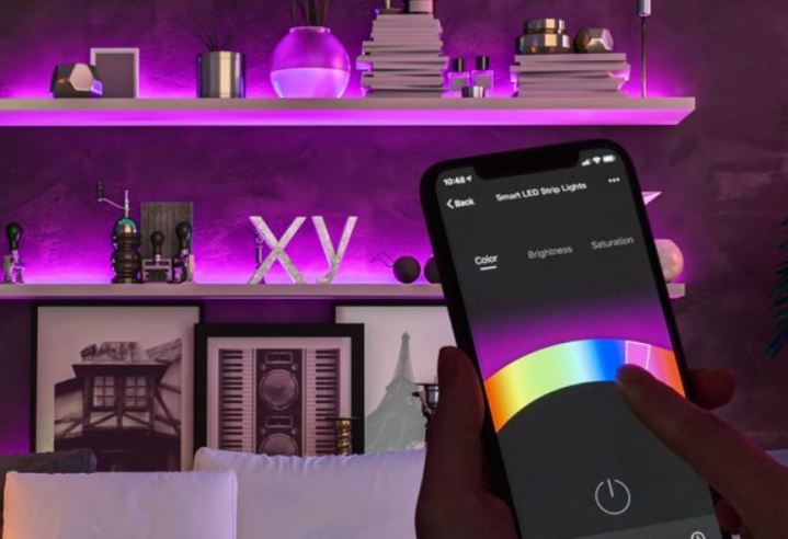 Smart LED strips light up a set of shelves in a purple hue while someone controls the color on a smartphone.
