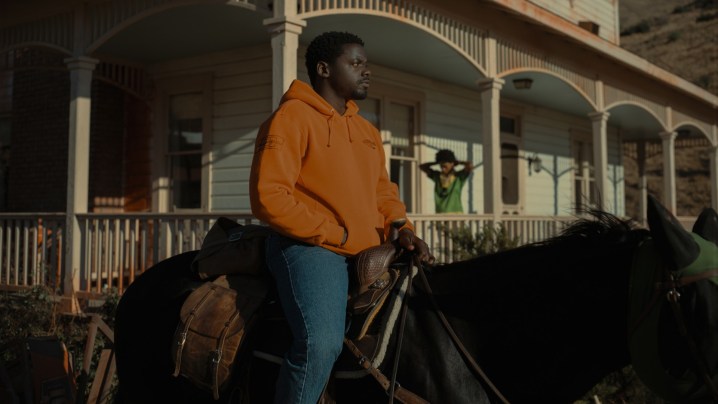 Daniel Kaluuya rides a horse in front of a house in a scene from Nope.