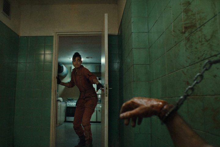 Ella Balinska looks toward a door and sees a bloodied, handcuffed hand in a scene from Netflix's Resident Evil series.