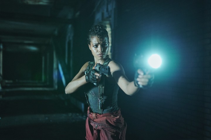 Ella Balinska holds a pistol and flashlight in the dark in a scene from the Resident Evil series.