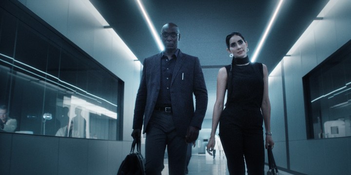 Lance Reddick and Paolo Nunez stand in a pristine, white hallway in a scene from the Resident Evil series.