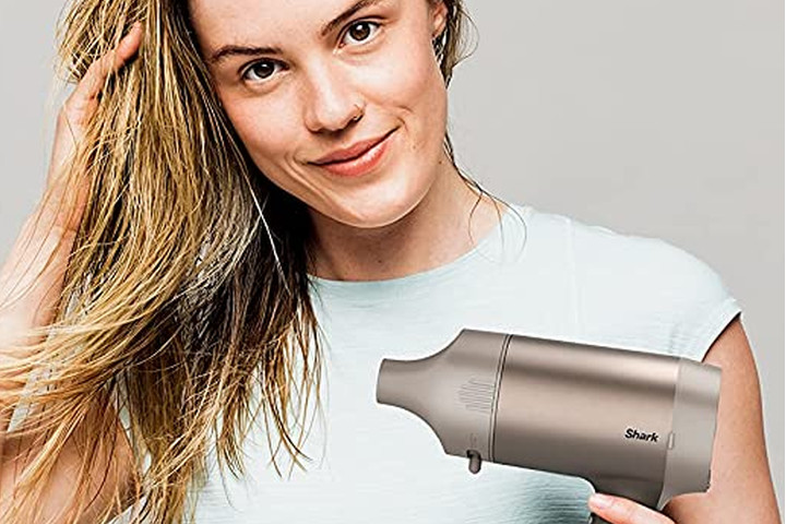 A woman wearing a white t-shirt uses the Shark HyperAir Hair Dryer to blow dry her hair.