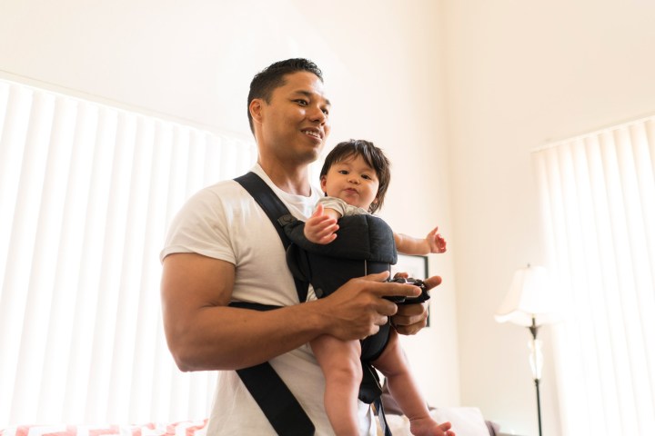 A father playing games with a baby in a baby carrier.
