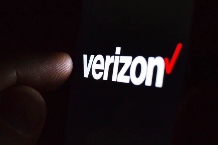 Verizon logo on a smartphone screen in a dark room and a finger touching it.