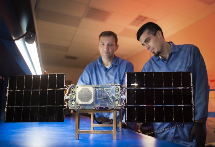 O primeiro de seis SunRISE SmallSats é mostrado aqui em uma sala limpa do Laboratório de Dinâmica Espacial da Universidade Estadual de Utah sendo trabalhada por engenheiros.  Apontado para a câmera está o lado voltado para o Sol do SmallSat, incluindo seus painéis solares totalmente implantados.
