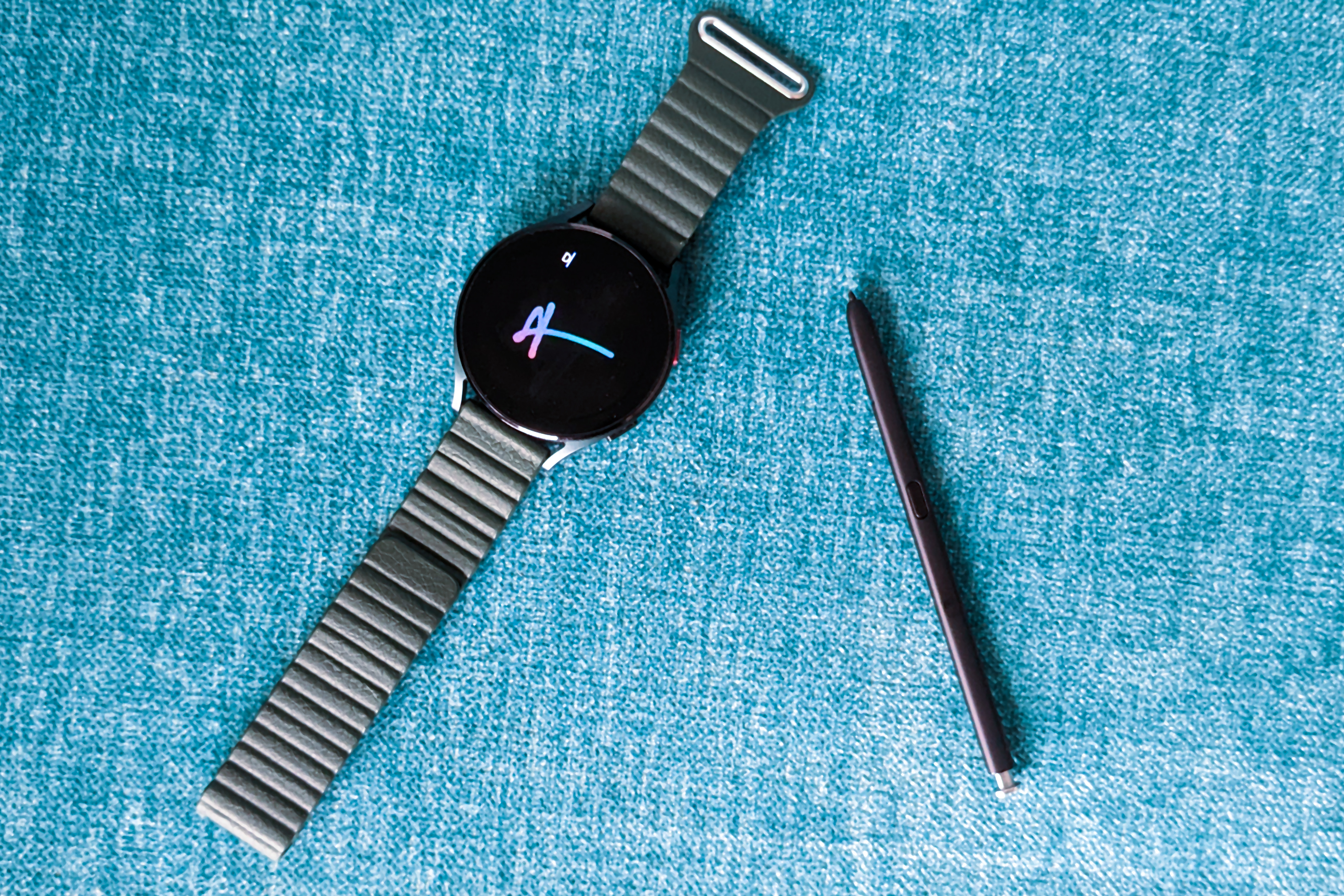 Samsung Galaxy Watch 4 com S Pen do Galaxy S22 Ultra em um fundo azul.