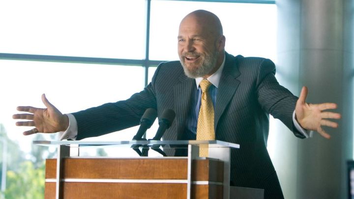 Obadiah Stane spreading his arms in joy while on a podium in Iron Man.